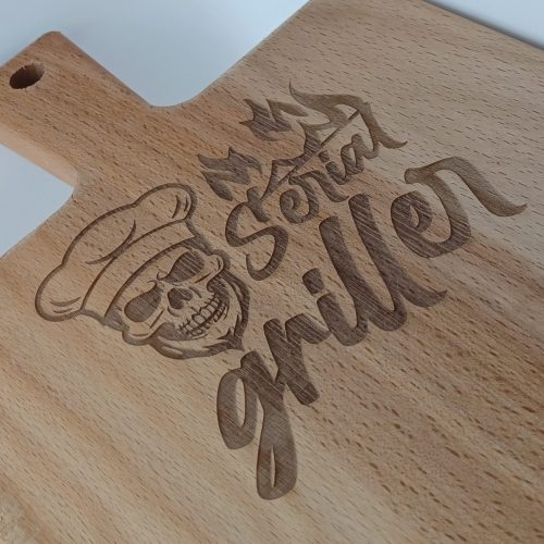 Close up borrelplank met gravure met een gravure erop van een doodshoofd en de tekst serial griller